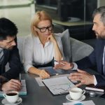 An image of 3 leaders looking at a dashboard of metrics. They are sitting at a table with coffee and papers discussing the report in front of them.